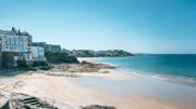 La plage de Dinard, près de Saint-Malo, avec son sable doré et ses eaux turquoises, bordée par d'élégantes villas et la côte rocheuse sous un ciel bleu éclatant.